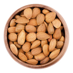 Shelled almonds in a bowl on white background. The raw edible seeds are no nuts, botanically they are drupes. Fruits in a wooden bowl, isolated, macro photo from above. Close up.