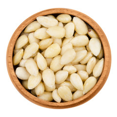 Blanched almonds in a bowl on white background. The raw edible seeds are no nuts, botanically they are drupes. Fruits in a wooden bowl, isolated, macro photo from above. Close up.