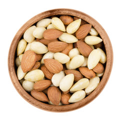 Blanched and shelled almonds in a bowl on white background. The raw edible seeds are no nuts, botanically they are drupes. Fruits in a wooden bowl, isolated, macro photo from above. Close up.