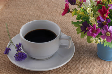 Obraz na płótnie Canvas Cup of coffee on sackcloth floor with flowers
