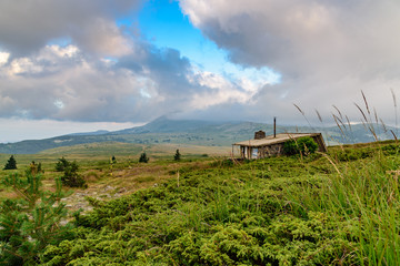 Fototapeta na wymiar Small stone cabin in the mountains, summer, clouds hanging over mountain top in the distance - Vitosha, Sofia, Bulgaria