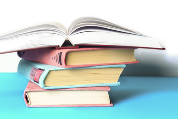 Open book, stack of colorful hardback books on light table. Back
