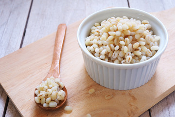 Close up of cooked barley in a white bowl on a wooden table.
