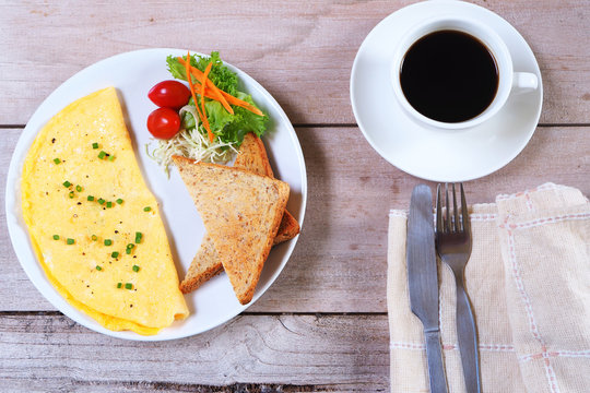 Top view of breakfast with omelette, tomatoes and and toast with black coffee on a wooden table.