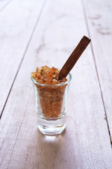 Close up of caramel sugar in a glass with cinnamon stick on a wooden background.