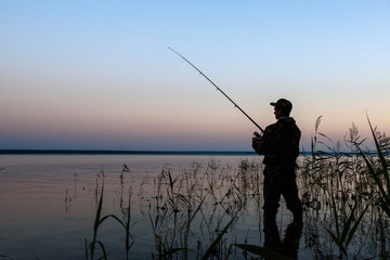 Fisherman silhouette at sunset on the lake while fishing   © river34