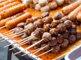 Grilled meat ball and sausage with sweet and spicy sauce at market. Local food in Thailand. (selective focus)