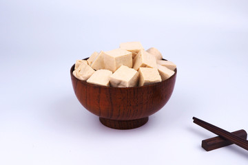 Close up of bean curd cube in a wooden bowl with white background.