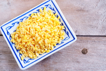 Top view of dried peeled split mung bean on a  square ceramic plate on a wooden background.