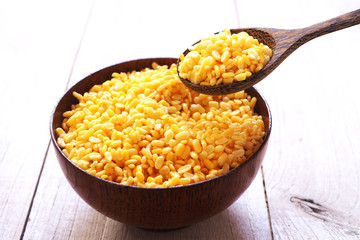 Close up of dried peeled split mung bean in a wooden bowl and spoon on a wooden background.