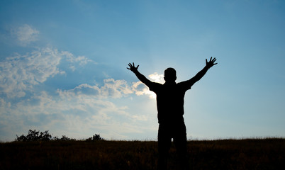 Silhouette of man worship with hands raised to the sky in nature