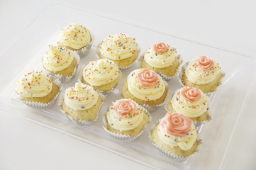 cupcakes with butter cream and multi-colored candy sprinkles in cups on a transparent tray on a white background