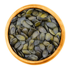 Pepita pumpkin seeds in a bowl on white background. Flat green edible summer squash seeds of Cucurbita pepo, genus Cucurbita, in wooden bowl. Isolated macro photo from above. Close up. Cucurbitaceae.