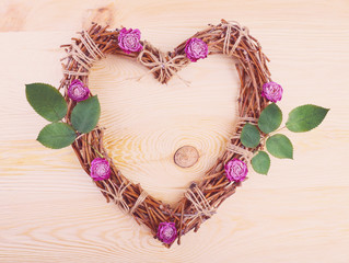 Wicker heart with dried roses and green leaves on wooden background