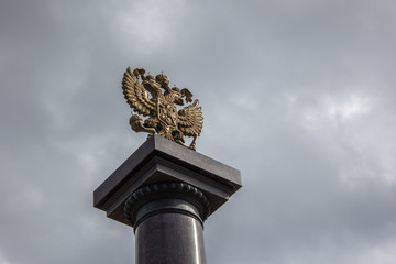 Fototapeta na wymiar Золотой герб Российской Федерации крупным планом на стелле на фоне облаков/