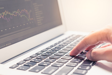 Woman hand typing on laptop keyboard with graph on screen