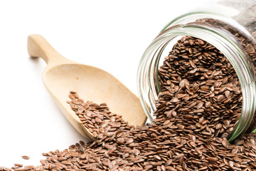 Linseed spilled from an overturned glass jar with a wooden spoon in the background isolated on white