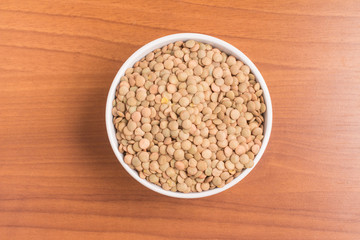 Raw Lentils into a bowl over a wooden table. (Lens culinaris)