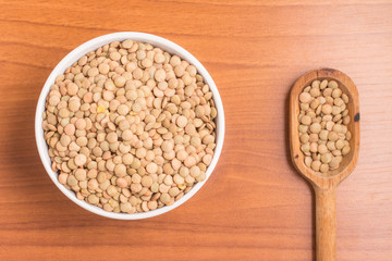 Raw Lentils into a bowl and spoon over a wooden table. (Lens cul