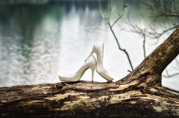 Białe buty ślubne stojące na starym drzewie na tle wody - obrazy, fototapety, plakaty
