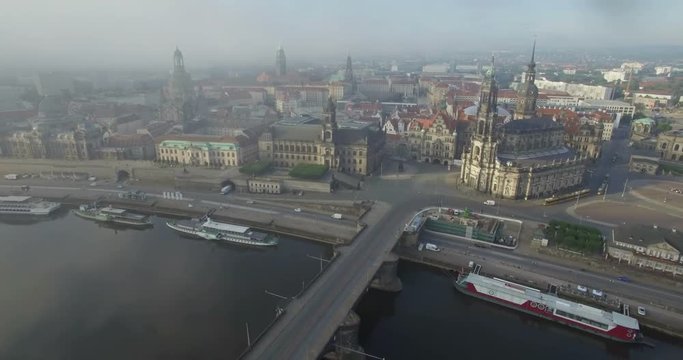 Aerial camera moves slowly over the Elbe River towards Katholische Hofkirche and the Augustusbruke in Dresden, Germany. Shot in 4k on a misty summer morning