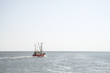Roter Krabbenkutter verlässt bei stiller See den Hafen der Nordseeinsel Pellworm