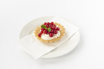 Delicious mini tart with fresh red currants and cream on white plate.