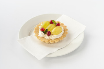 Delicious mini tart with fresh red currants, grapes and cream on white plate.