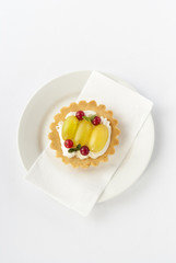 Delicious mini tart with fresh red currants, grapes and cream on white plate. Vertical.