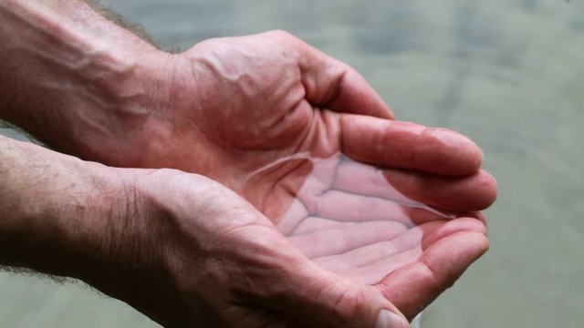 Man taking clear water at a lake by hands
