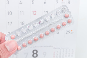Close up hand hold birth-control pill with date of calendar background, health care and medicine...