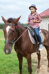 Obraz premium Young girl in a plaid shirt and hat sitting on horseback