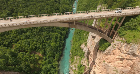 Durdevica concrete arch bridge with cars driving and crowd of people watching at Tara River canyon, Montenegro. Aerial view from drone