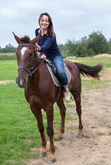 Joyful young woman touching her chestnut horse while riding on field