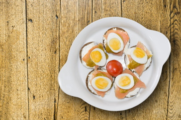 Mini sandwiches with dark bread with salmon eggs and yogurt on white ceramic plate. View from above.