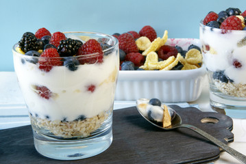 Easy summer dessert for breakfast or a snack: cereal, oatmeal, fruit, yogurt. Dessert tasted: a spoon full of it. Plate with berries and another glass with dessert in the background. Rustic table.