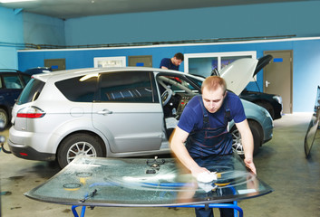 Automobile glazier cleaning car windscreen or windshield in service garage