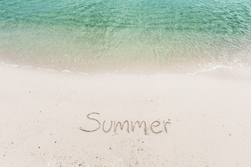 Word Summer handwritten on sandy beach with soft ocean wave on background