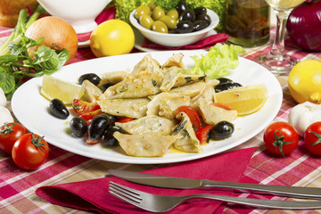 Prepared cod pieces in sauce, cherry tomatoes, black olives and lemon served on a white plate.
