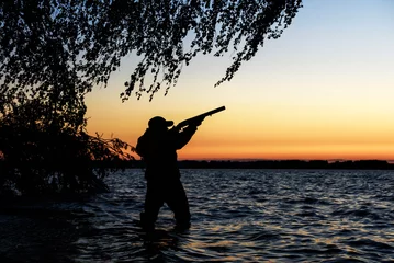 Papier Peint photo autocollant Chasser Hunter silhouette at sunset, while hunting on the lake  