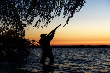 Hunter silhouette at sunset, while hunting on the lake  