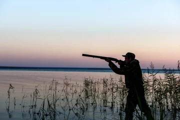 Garden poster Hunting Hunter silhouette at sunset, while hunting on the lake  