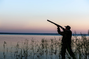Hunter silhouette at sunset, while hunting on the lake  