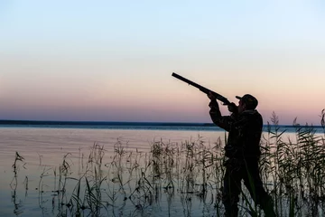 Foto auf Acrylglas Jagd Jägersilhouette bei Sonnenuntergang, während der Jagd auf dem See