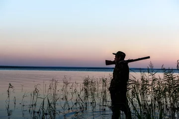 Papier Peint photo autocollant Chasser Silhouette de chasseur au coucher du soleil, tout en chassant sur le lac