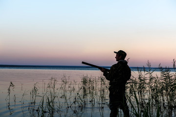 Hunter silhouette at sunset, while hunting on the lake
