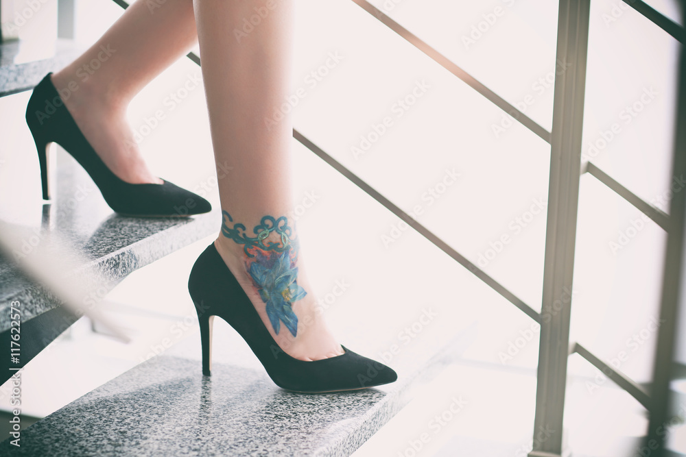 Poster Woman with tattoo on her leg in high heeled shoes on the stairs