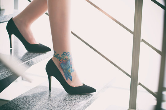 Woman with tattoo on her leg in high heeled shoes on the stairs