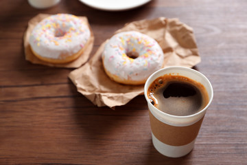 Paper cup of coffee and doughnuts on wooden background
