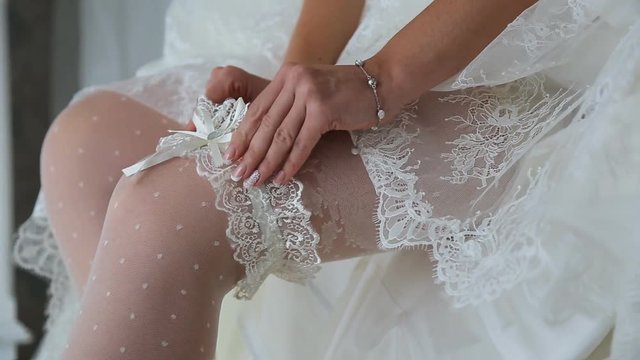 Young fiancee puts on her left leg garnment sitting on bed.